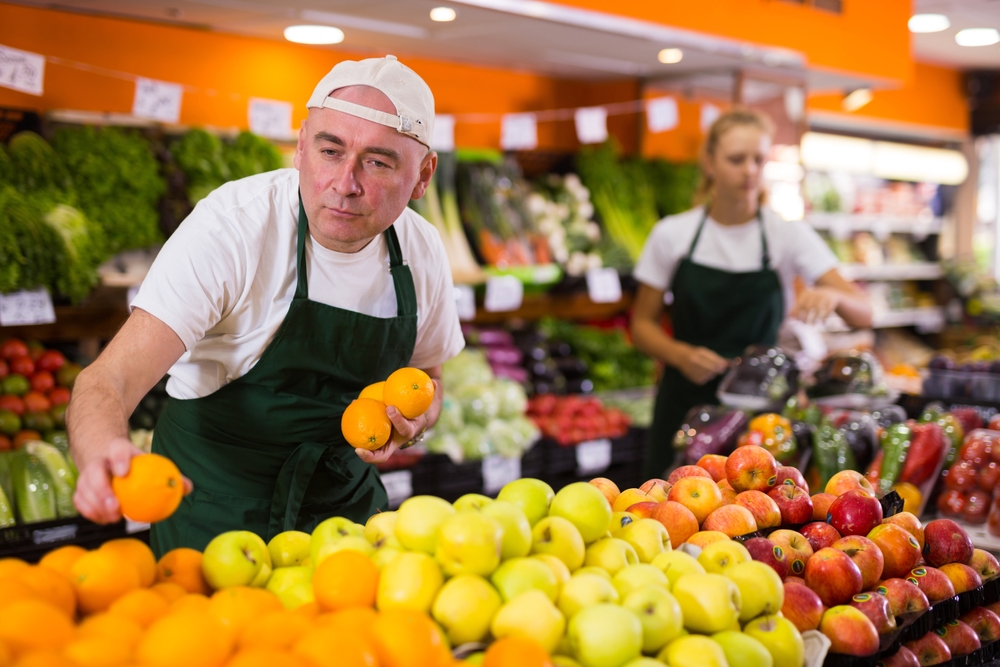 Man and woman supermarket workers reorganise fruit display